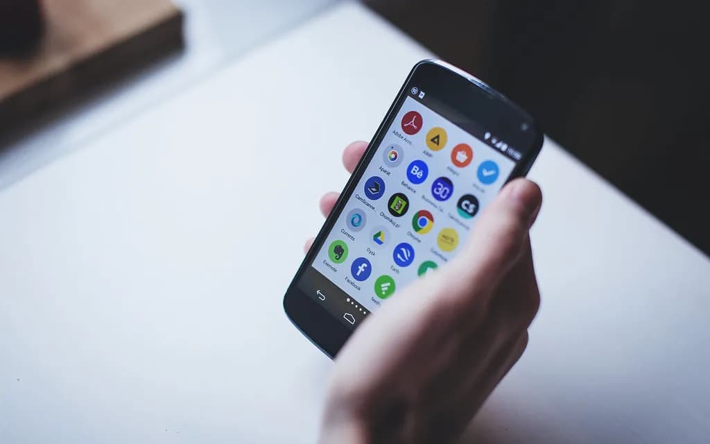 Mão segurando um celular com a tela de aplicativos aberta