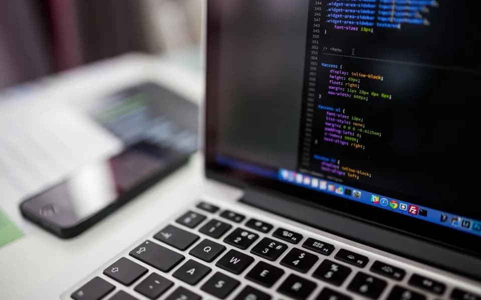 Notebook com código na tela e um celular ao lado